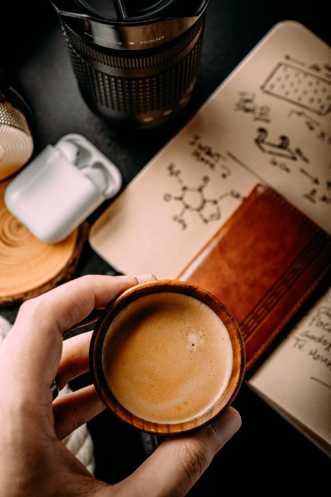 Hand holding espresso over a notebook and creative workspace